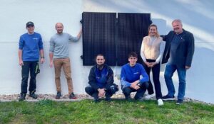 Ein Solarkraftwrek ist an eine weiße Hauswand montiert. Davor stehen die Handwerker, der Stifter der Anlage, sowie die verantwortliche Lehrkraft im Schullandheim Riedenburg und der Geschäftsführer,