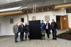 Menschen stehen vor einem Haus, in der Mitte ein Solar-Modul.
